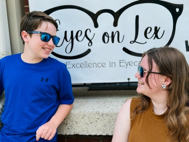 Smiling boy and girl wearing sunglasses in front of Eyes on Lex sign